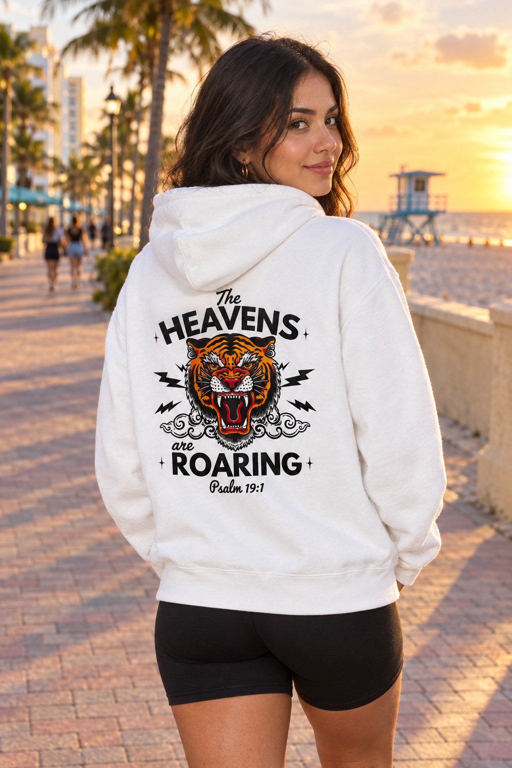 Woman wearing white The Heavens Are Roaring Psalm 19:1 hoodie on the Hollywood Beach Broad