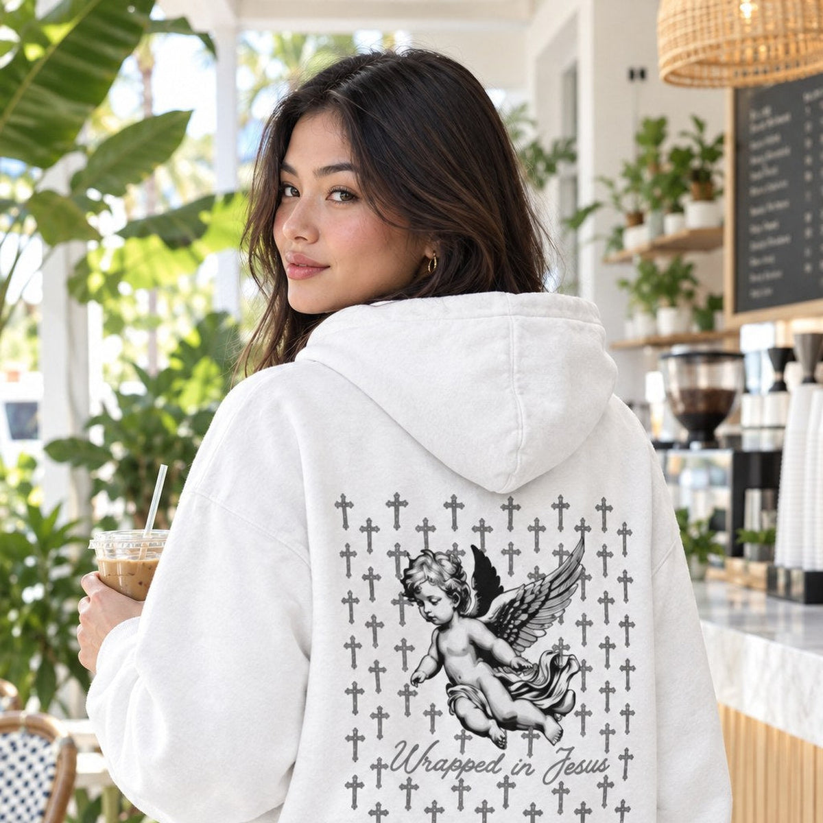 Woman wearing white Angel hoodie with praying angel and cross back graphic in a Palm Beach coffee shop