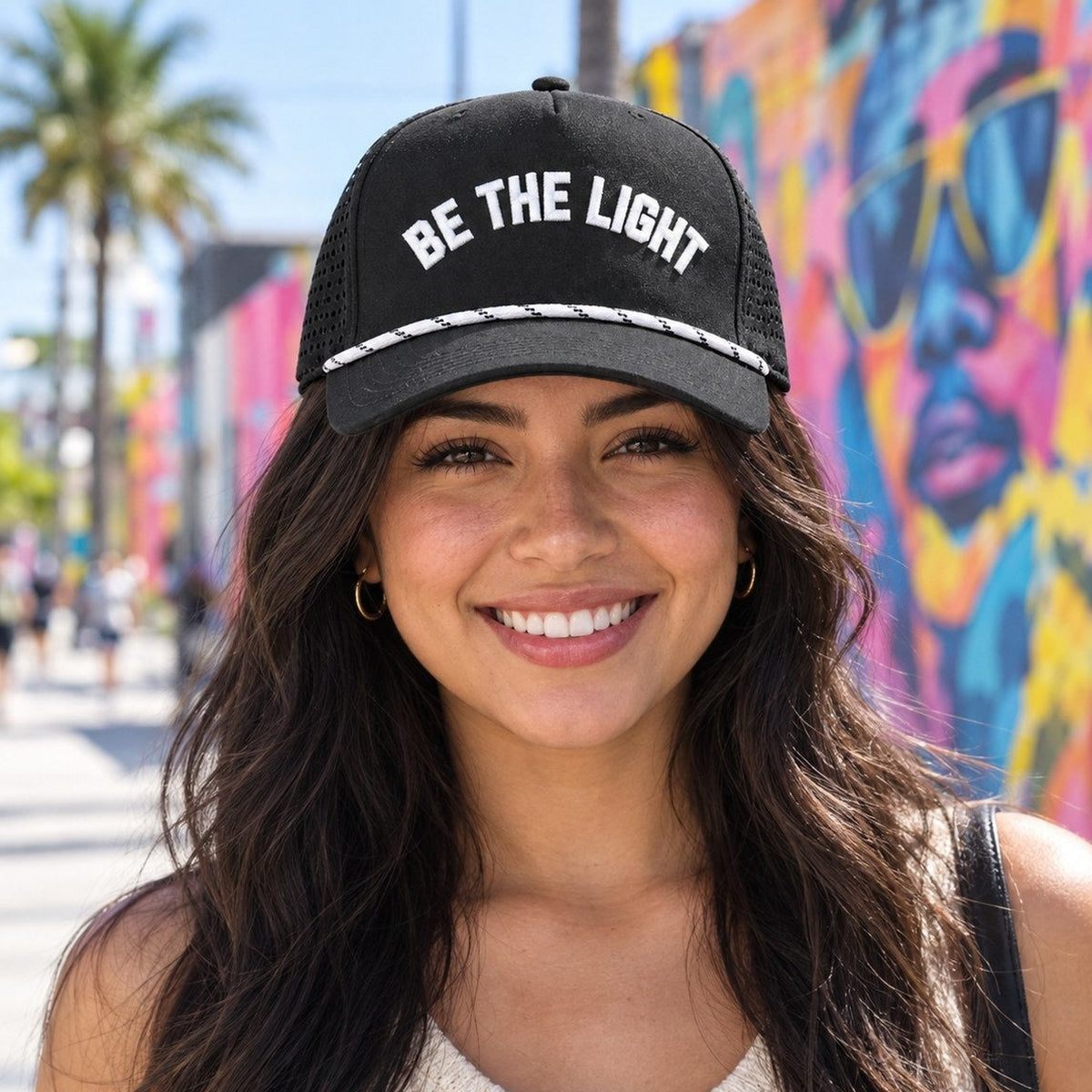 Woman wearing black Be The Light Christian rope hat on a Miami mural street