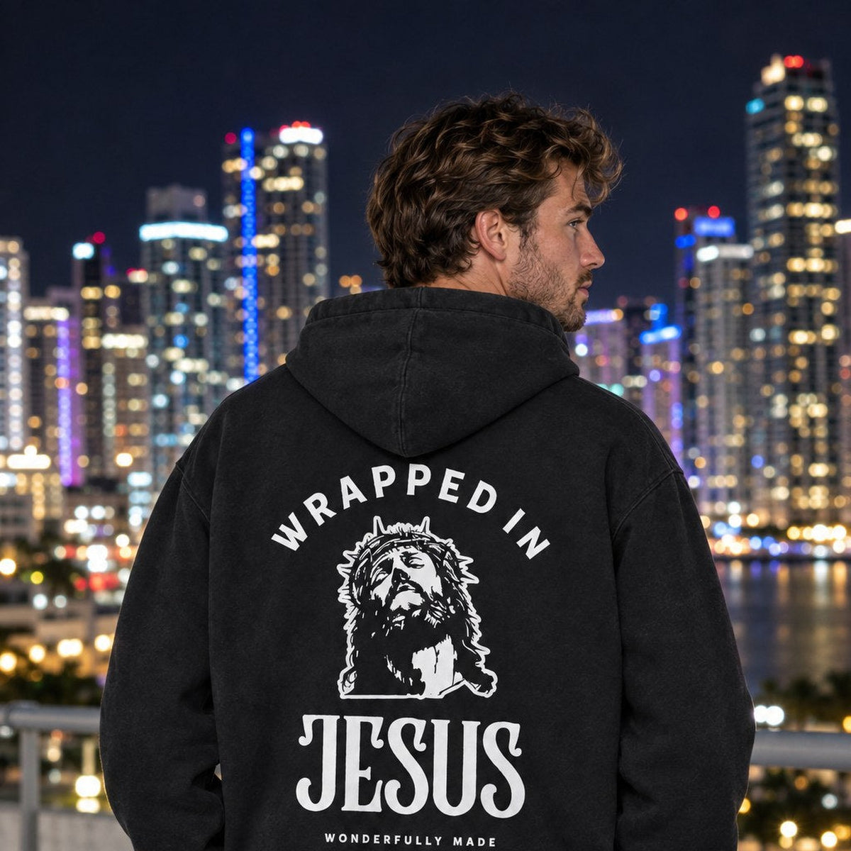 Man wearing black Crown of Thorns Wrapped In Jesus hoodie on a Miami rooftop at night, graphic view