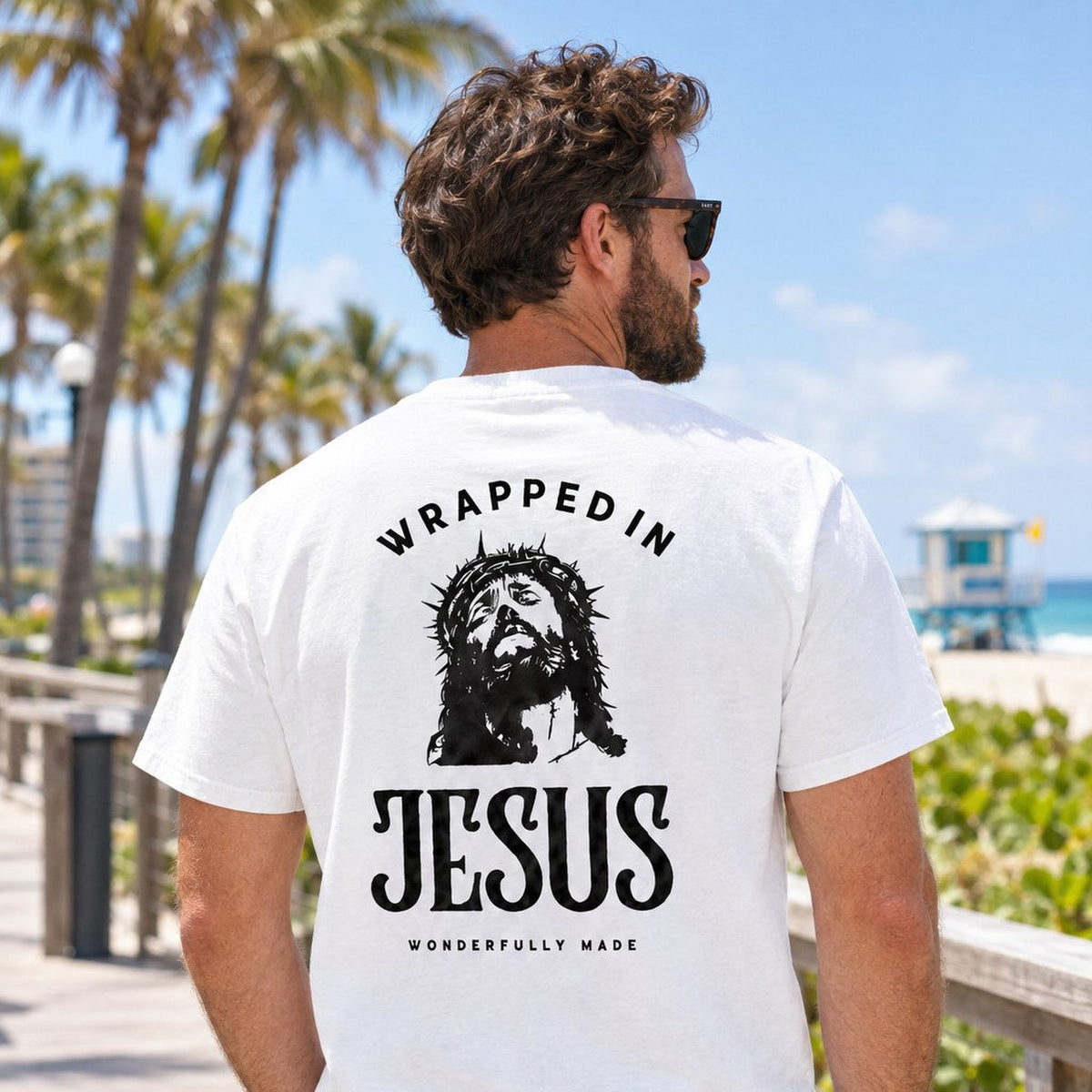 Man wearing white Crown of Thorns Wrapped In Jesus tee on a Boca Raton beach boardwalk, back graphic view
