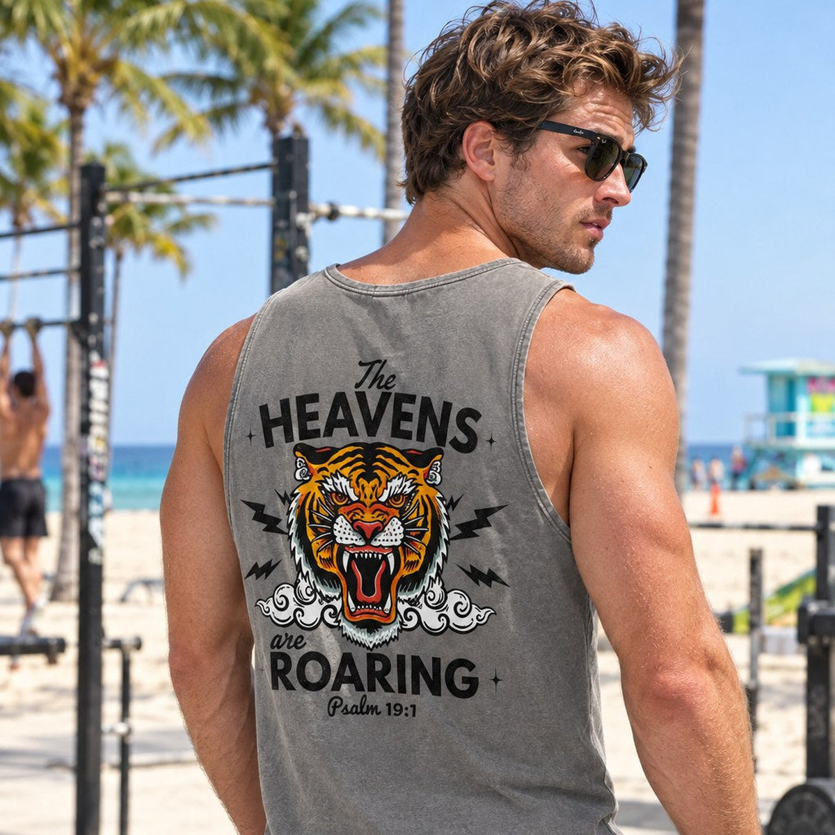 Man wearing gray The Heavens Are Roaring Psalm 19:1 tank top at an outdoor beach gym, back graphic view