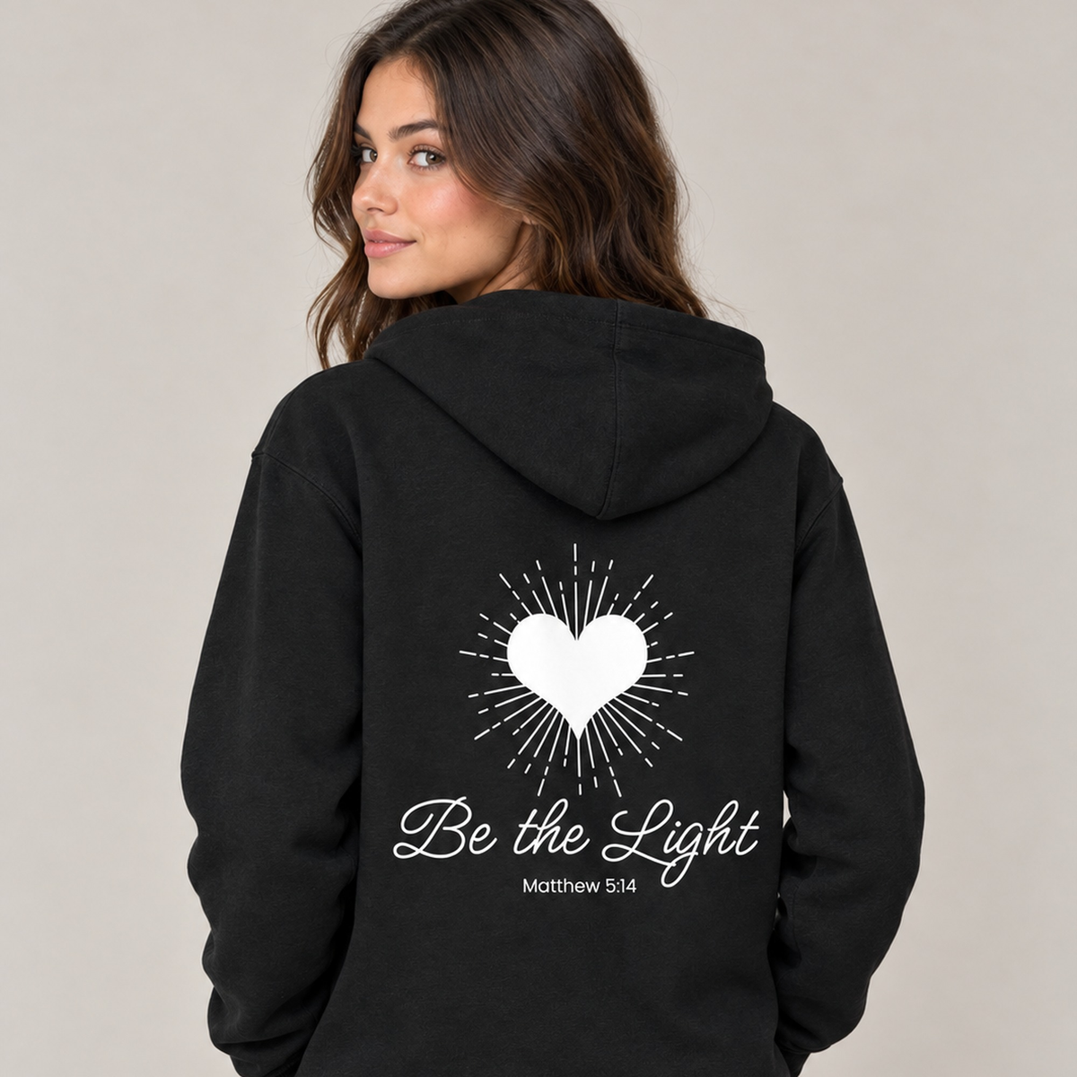 Woman wearing black Be The Light zip-up hoodie, back view with Matthew 5:14 design