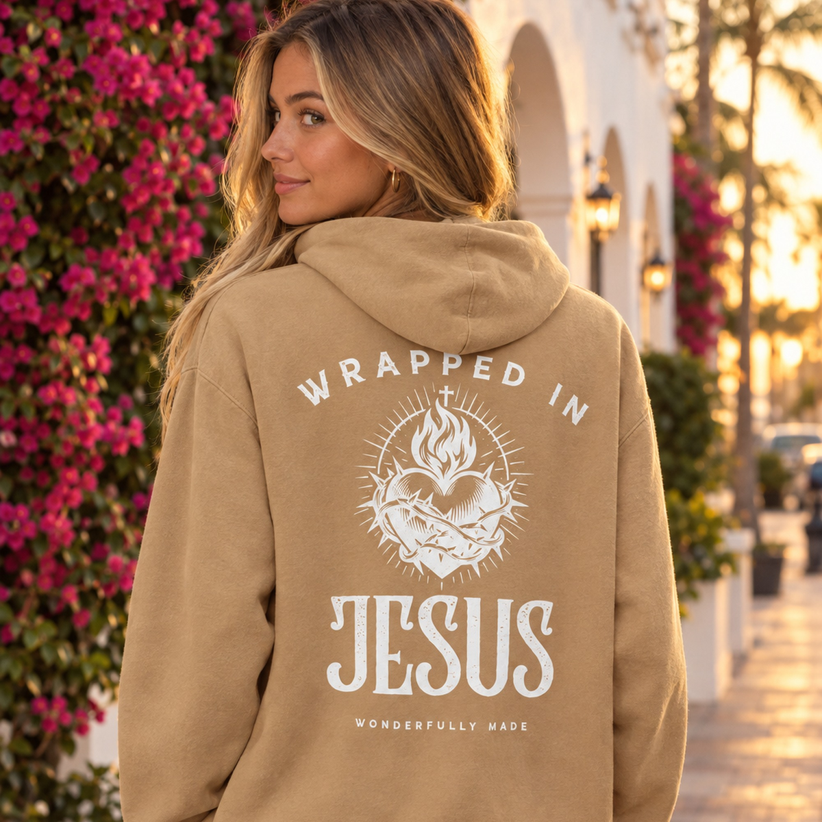 Woman wearing burro tan Sacred Heart oversized hoodie on a Palm Beach street with bougainvillea